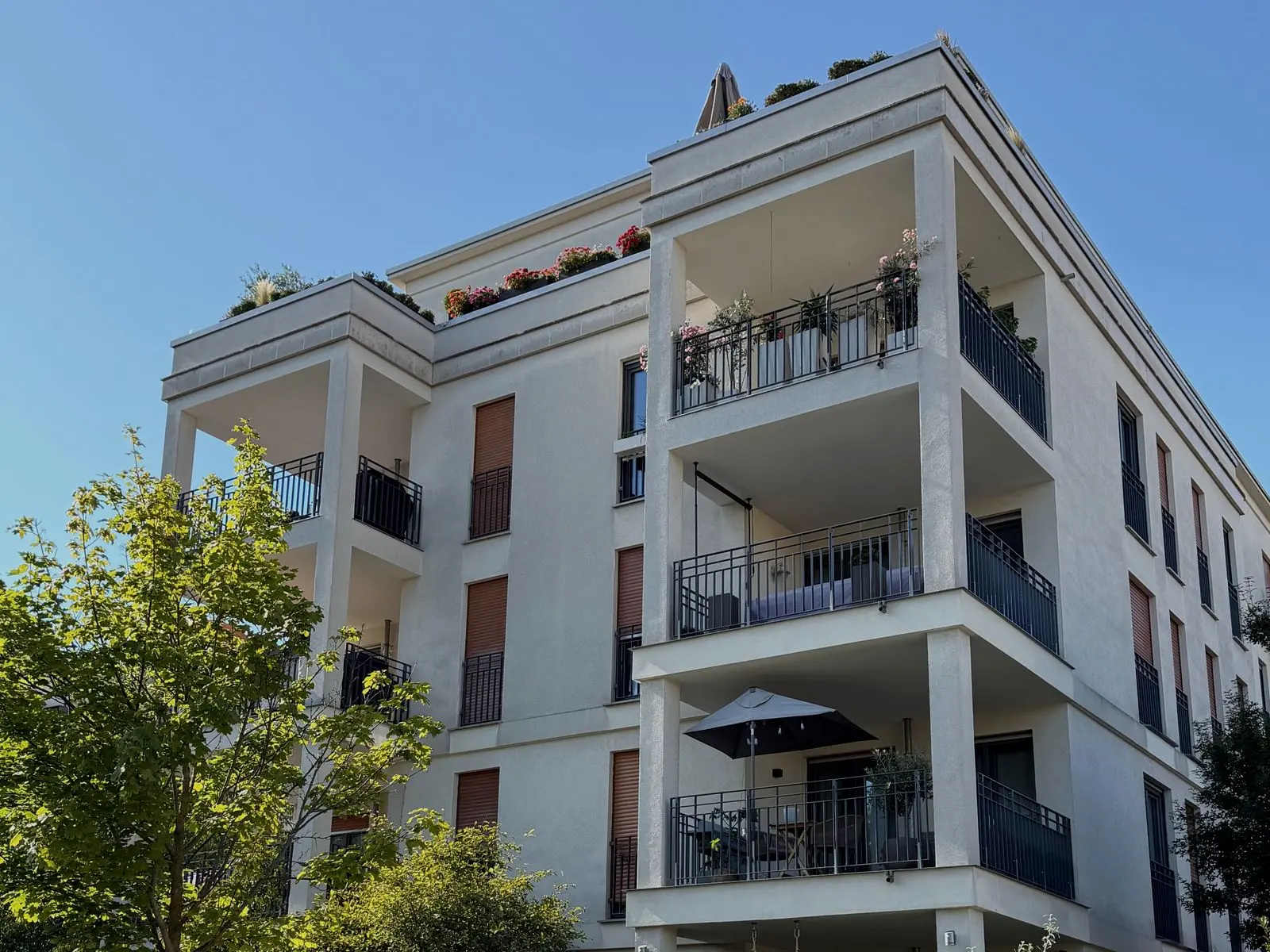 Well-kept white apartment building with planted balconies behind a neatly trimmed hedge